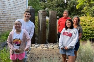 Three kids and two adults hold a sign that says Welcome to The Alexandra Ellis Caring Cabin