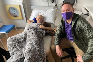 A teenage boy in a hospital bed being visited by a man