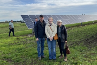 Three people standing on a farm with solar panels behind them