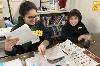 An adult and child smiling while sorting through sheets in a binder, including Bingo