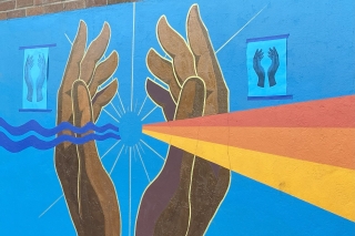 Artwork of two hands painted on a brick wall