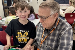 An older man volunteer with a young student and a workbook