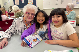 An older woman volunteer reading with two young students