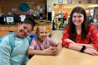 A young volunteer sitting at a table with two children
